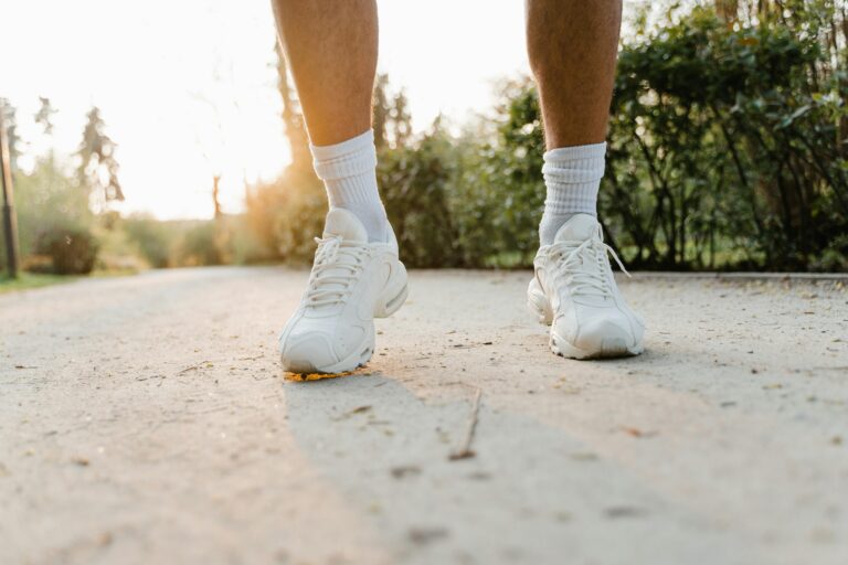 Close-up of legs wearing white sneakers walking on a sunlit path outdoors.