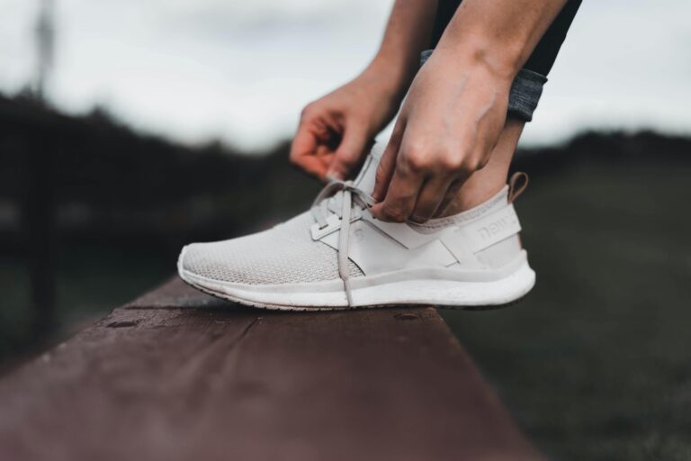 A focused shot of hands tying shoelaces on a sneaker on a bench outdoors.